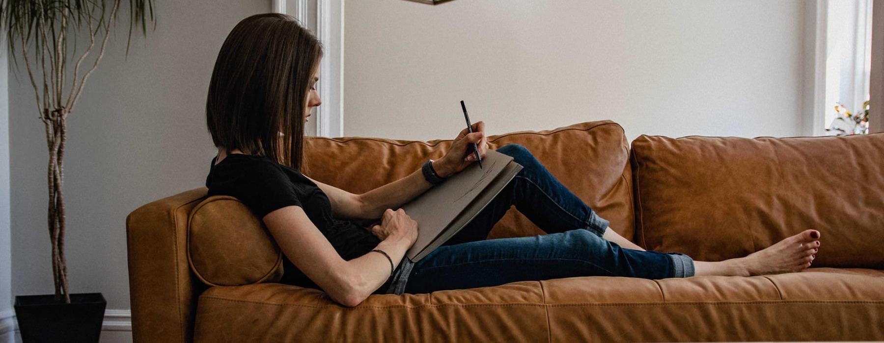 woman lies on a couch and draws on a large sketch pad
